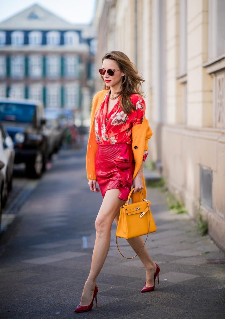 Alexandra Lapp wearing Hawaiian Silk Blouse in a kimono shape with all-over print by Jadicted, the Evangelista knitted cardigan by Ganni in turmeric orange, ruffled mini skirt in red leather by Magda Butrym, a Hermes Kelly bag in orange, Gianvito Rossi red patent pumps and gold mirrored Thom Browne sunglasses in red on May 6, 2018 in Duesseldorf, Germany.